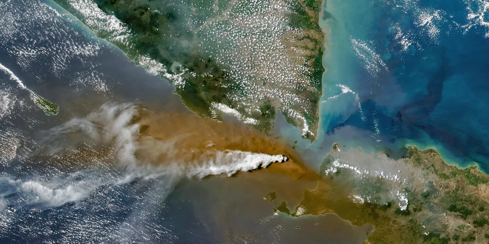 Satellite view of Anak Krakatau erupting in the Sunda Strait, with a brown ash plume spreading east across the sea toward Java and Banten.