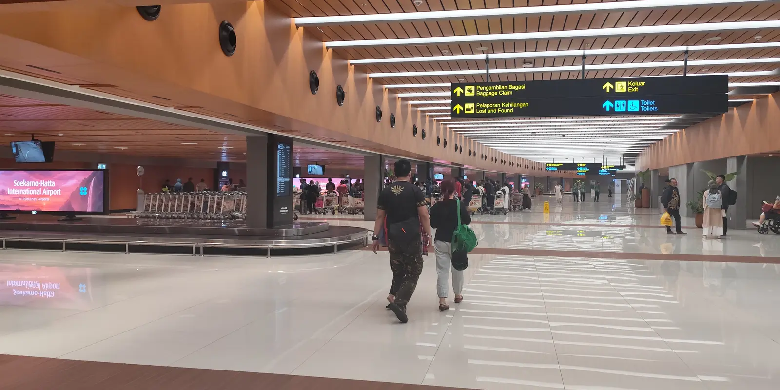 The arrivals hall of the revitalised Terminal 1C at Soekarno-Hatta, with baggage carousels, bilingual overhead signage and polished floors.
